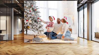 African American family in Santa hat celebrate New Year together at home and decorate Christmas tree, teenage boy celebrates New Year with mom and dad and holds red toy Wall mural