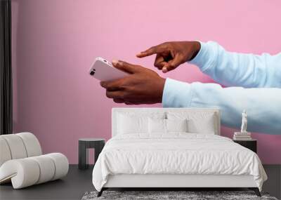 african american male hands hold smartphone and choose point finger at the screen on pink isolated background Wall mural