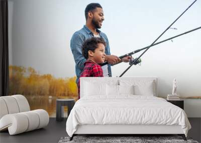 African American man and child standing on wooden pier holding fishing rods on the river, dad teaching his son to fish in the lake, family resting and relaxing on the weekend Wall mural