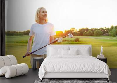 An elderly woman with a smile on her face is standing on a golf course holding a golf club. He is happy, enjoying his hobby  Wall mural