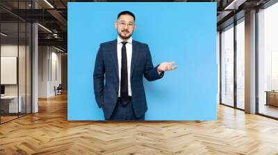 asian businessman in suit and glasses shows his hands to the side, korean entrepreneur advertises copy space Wall mural