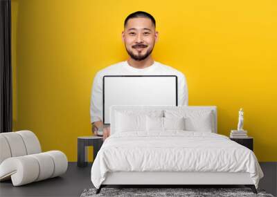 asian man in white t-shirt shows blank laptop screen on yellow isolated background Wall mural