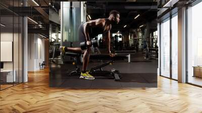 athletic african american man trains in dark gym, athletic guy lifts heavy dumbbells in fitness club Wall mural