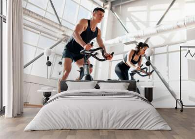 athletic couple of cyclists train on static bicycle simulator, man trainer and fitness woman go in for sports together Wall mural