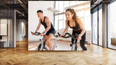 athletic couple of cyclists train on static bicycle simulator, man trainer and fitness woman go in for sports together Wall mural