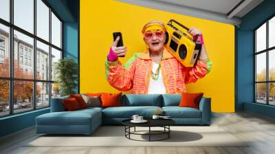 crazy old grandmother with tape recorder and smartphone in hipster clothes listens music on yellow background Wall mural