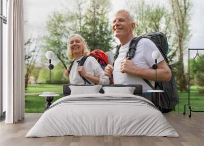 elderly athletic couple of seniors man and woman with hiking backpacks travel in the forest outdoors, gray-haired grandparents go hiking in nature Wall mural