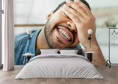 happy african american man with braces closes his eyes with his hand and shows facepalm in a white cafe, the man is embarrassed by a mistake and smiles Wall mural