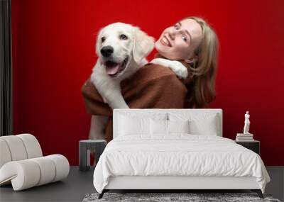 happy cheerful beautiful girl holding a dog on a red background, a woman hugs a golden retriever puppy and smiles, people with pets Wall mural