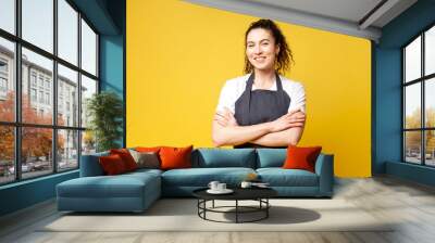 portrait of young barista girl in uniform on a yellow background, a woman waiter stands with crossed arms Wall mural