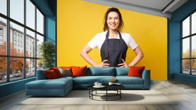 portrait of young barista girl in uniform on a yellow background, woman waiter in denim apron smiling Wall mural