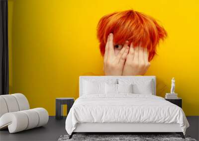 scared red-haired child boy hiding and covering his face with his hands on a yellow isolated background, excited teenager with orange hairstyle afraid and peeking Wall mural