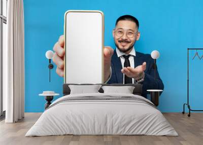 successful asian businessman in suit and glasses shows blank smartphone screen on blue isolated background Wall mural