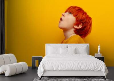 surprised red-haired child boy looking up with open mouth on yellow isolated background, shocked teenager with orange hairstyle looking at copy space in amazement Wall mural