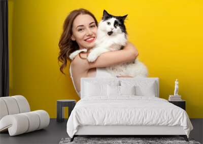 young cute girl holding black and white cat on yellow isolated background and smiling, woman with pet Wall mural