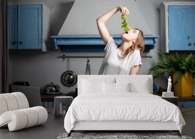 young girl prepares a vegetarian salad in the kitchen, she looks into a laptop and eats greens, eating healthy foods Wall mural