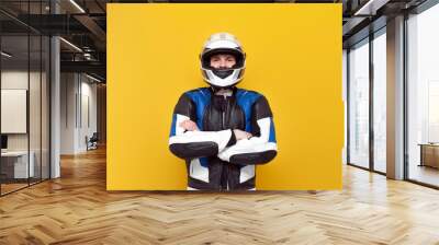 young guy motorcyclist in leather jacket and helmet stands with his arms crossed on yellow isolated background Wall mural