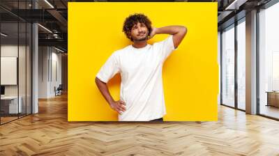 young indian puzzled guy thinks and remembers and scratches his head on yellow isolated background Wall mural