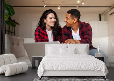 young multiracial couple sitting on comfortable sofa and looking into laptop at home Wall mural