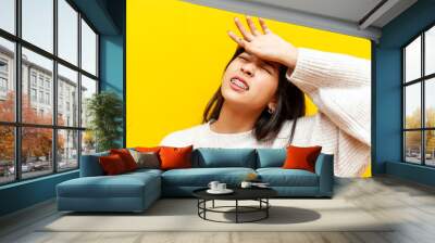 young tired asian woman with braces suffers and is sad on a yellow isolated background, korean unhappy girl wipes her forehead with her hand and shows dissatisfaction Wall mural