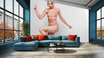 Slim young woman in sport outfit, tight colorful leggings and top with geometrical patterns in a motion, happy, joyful, jumping, isolated in studio Wall mural