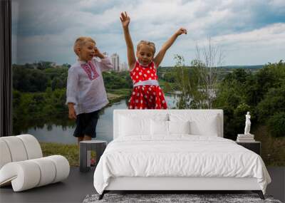 two carefree children, a boy and a girl dancing on a hill above the river Wall mural