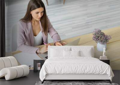 Young businesswoman in a pink jacket is working on a laptop on a large wooden table. Communicates with the client in the messenger chat. Distant work. Wall mural