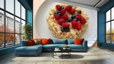 Ripe dark blue blueberries and red raspberries lie in a heap in a texture gray round plate on top of boiled oatmeal, close-up, top view. Plate with food on a peach surface. Proper nutrition. Vitamins. Wall mural