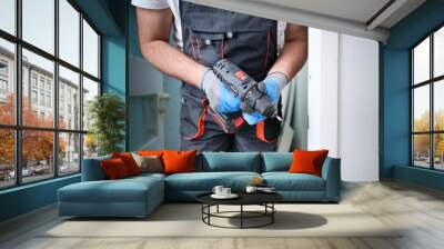 Construction worker holding electric cordless screwdriver in hand at construction site. Accessories for assembling, install furniture, repair home. Home renovation, electric tool for job. Crop view. Wall mural