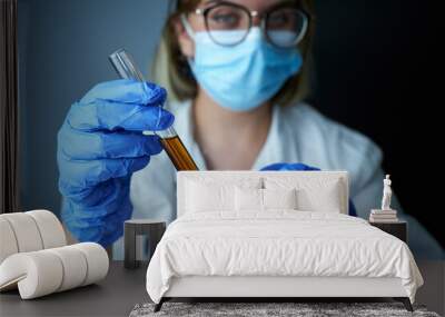 Pretty female tech or scientist holding  liquid sample in test tube . Laboratory worker in blue gloves holding test tube with blood sample, closeup. Wall mural