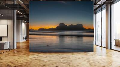 Beautiful tropical twilight after sunset. The dark blue sky is highlighted with orange at the horizon. Silhouettes of picturesque mountains in the distance. Reflection on the surface of a calm ocean. Wall mural