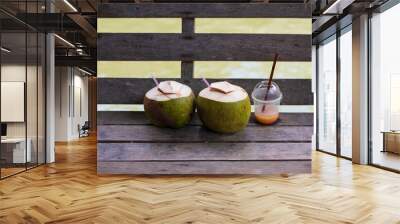 Two young coconut drinks and empty plastic fruit smoothie cup on wooden bench. Background about the problem of environmental pollution. Social problem with waste accumulation. Wall mural