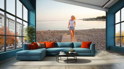 Hot blond woman running on the uninhabited beach. the lifestyle of people are the happiness vacation. Girl dressed jeans  short and t-shirt. Wall mural