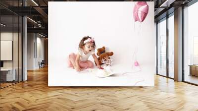 Two years old female kid celebrate the birthday. The girl blows out candle on the cake against thr background of a white wall in the studio with pink balls of star Wall mural