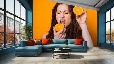 Beautiful girl on a bright yellow background. Model with fruit in hand. Two orange slices.  emotion. Crooked faces Wall mural