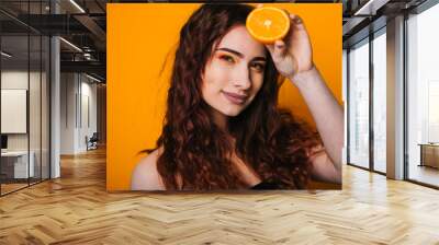 Beautiful girl on a bright yellow background. Model with fruit in hand. Two orange slices. Wall mural