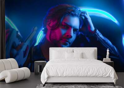 Handsome man in cyberpunk style with a machine gun in his hands in the dark. A guy in a leather jacket in the scenery of the future in neon color. Spaceship. Wall mural