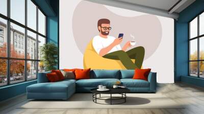 a man sits on an armchair (bean bag) with a phone and a cup of coffee Wall mural