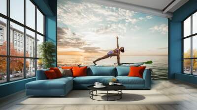 Young woman doing YOGA on a SUP board in the lake at sunrise Wall mural