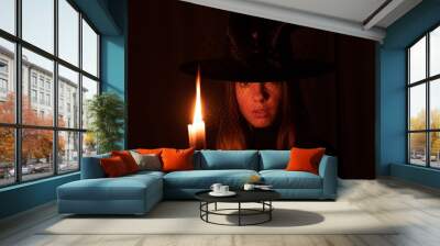 A girl in a witch's hat with a candle in her hands in the dark, a witch and a flame of a switch in the dark, halloween, magic Wall mural