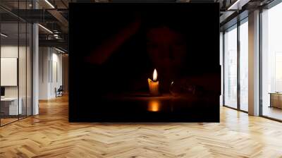 A girl in the dark sits with candles and a light bulb at a table in the dark at home, people without light Wall mural