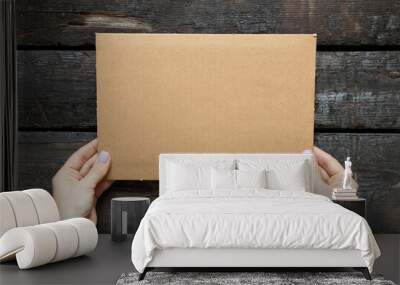 A woman's hand holds a cardboard box in her hands on a wooden background, space for text, a cardboard box in her hands Wall mural