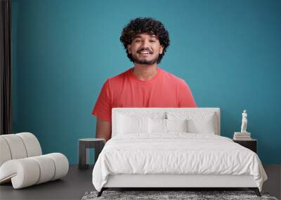 Young smiling confident happy Indian man 20s in basic coral t-shirt hold look camera isolated on a blue studio background portrait. People lifestyle concept. Wall mural