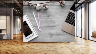 White notebook with two pencils shot from above on a wooden light table next to a cotton branch, a golden laptop and a phone Wall mural