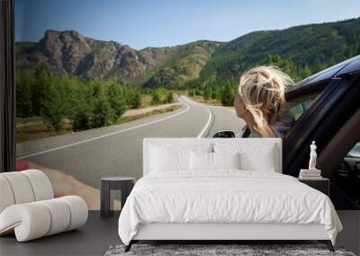 A blonde woman with her head out the window enjoying a scenic drive through the sawtooth mountain. Sun is shining. Shoot from the back Wall mural