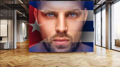 A portrait of a young serious man, in whose eyes are reflected the national flags  Cuba, against an isolated black background and flag Wall mural