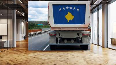 Big dirty truck with the national flag of Kosovo moving on the highway, against the background of the village and forest landscape. Concept of export-import,transportation, national delivery of goods Wall mural