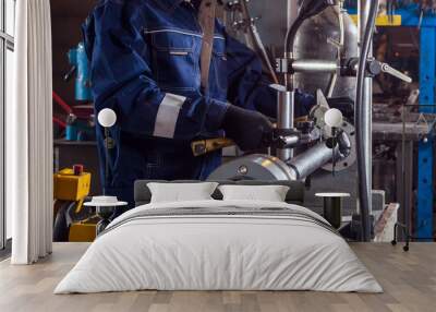 Close-up of a male auto mechanic in blue uniform works with a mettalic hammer on an automatic welding machine for the repair of cardan shafts Wall mural