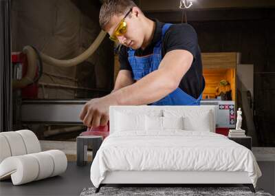 Portrait of a  young man  carpenter using electric sanding machine to polish a wood barin workshop Wall mural