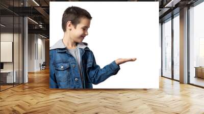 Portrait of smiling boy in denim jacket demonstrates with hand and looks at her, having fun on white isolated background Wall mural